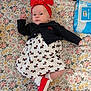 baby, baby_clothes, black_jacket, cute, expression, face, floral_bedspread, hand_raised, headwear, indoor, infant, lying_down, pack_of_wipes, patterned_clothing, person, red_headband, red_shoes, small_footwear, soft_lighting, white_dress