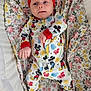 baby, blanket, child, colorful_clothing, cute, floral_blanket, headband, indoors, infant, lying_down, mickey_mouse, newborn, onesie, patterned, portrait, red_bow, sleepwear, small_hands, soft_toys, white_socks