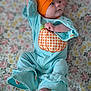 baby, infant, child, blue_onesie, orange_headband, bow, pumpkin_applique, striped_clothing, floral_blanket, lying_down, barefoot, cute, curious, portrait, indoors, soft_lighting, smiling, small_hand, small_foot, comfortable