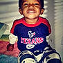 bed, blanket, casual, child, clothing, cute, happy, indoor, mickey_mouse, pants, person, portrait, shadow, shirt, sitting, smiling, texans, toddler, wall, young_child