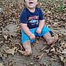child, toddler, baby, outdoor, autumn, fallen_leaves, nature, portrait, sitting, smiling, happy, face, person, blue_shirt, blue_shorts, barefoot, playful, grass, dirt, daylight