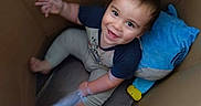 Aaron joined the competition — help win amazing prizes! baby, child, smiling, happy, portrait, indoor, cardboard_box, sitting, lying_down, waving, blue_pillow, toy, colorful, casual_clothing, short_hair, barefoot, candid, photography, warm_lighting, playful