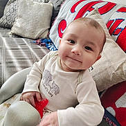 Wroen is registered to the contest to win money with this photo: baby, baby_seat, blanket, child, clothing, comfort, couch, cute, face, hand, happy, home, indoors, infant, person, pillow, portrait, smile, toy, young_child