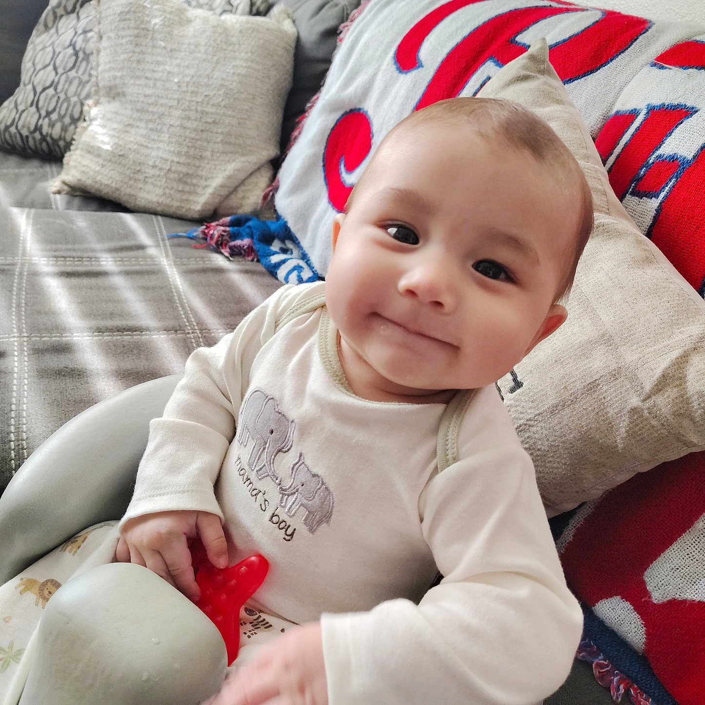 Wroen is registered to the contest to win money with this photo: baby, baby_seat, blanket, child, clothing, comfort, couch, cute, face, hand, happy, home, indoors, infant, person, pillow, portrait, smile, toy, young_child