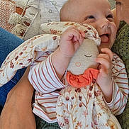 Charlie participe au concours pour gagner de l'argent avec cette photo : baby, child, plush_toy, stuffed_animal, person, hand, face, smiling, tongue_out, striped_clothing, floral_pattern, blanket, cuddle, holding, close_up, indoor, happy, affection, human, comfort