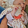 baby, child, plush_toy, stuffed_animal, person, hand, face, smiling, tongue_out, striped_clothing, floral_pattern, blanket, cuddle, holding, close_up, indoor, happy, affection, human, comfort