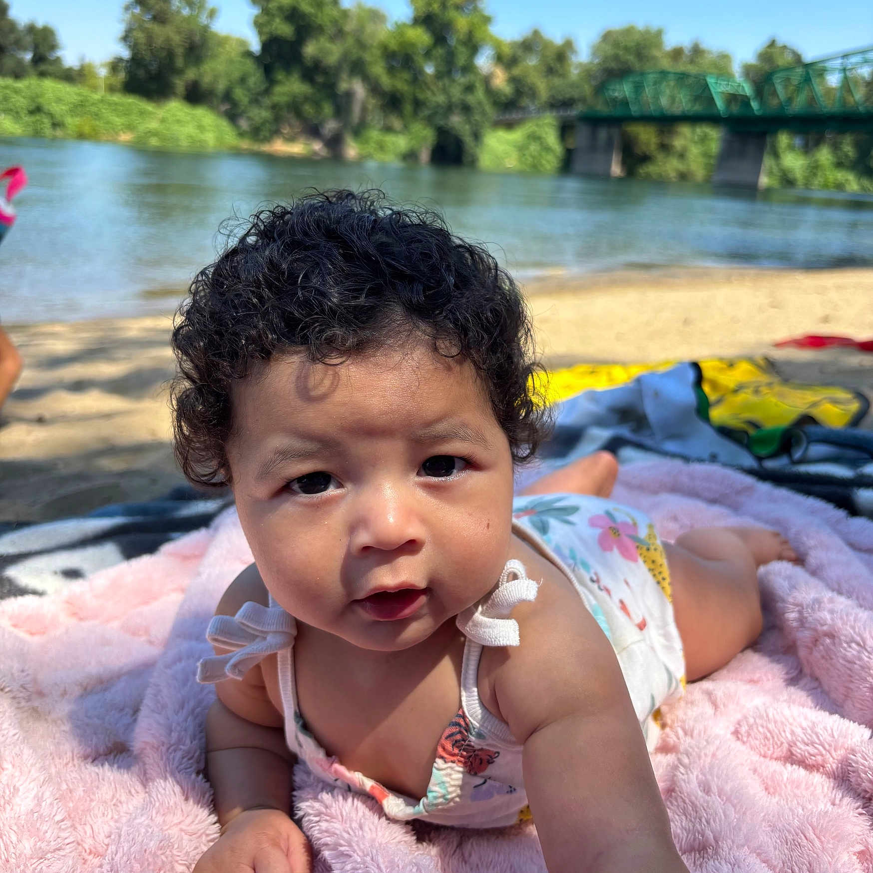 Zaiyla joined the competition — help win amazing prizes! baby, beach, blanket, blue_sky, bridge, child, curly_hair, cute, infant, nature, outdoor, person, portrait, reaching, river, sand, summer, sunlight, trees, water