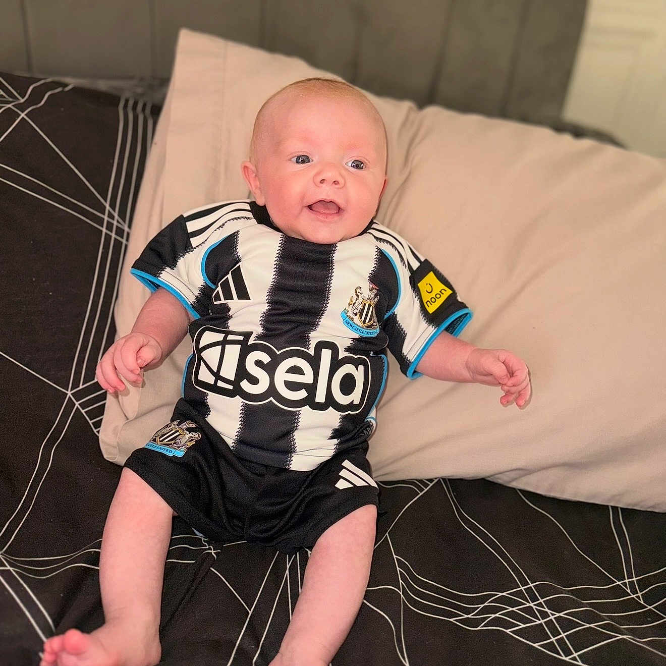 Ronniejay is registered to the contest to win money with this photo: baby, bed, black_and_white, child, clothing, cute, face, feet, hands, happy, head, indoors, infant, person, pillow, smiling, soccer_jersey, sportswear, striped_shirt, young