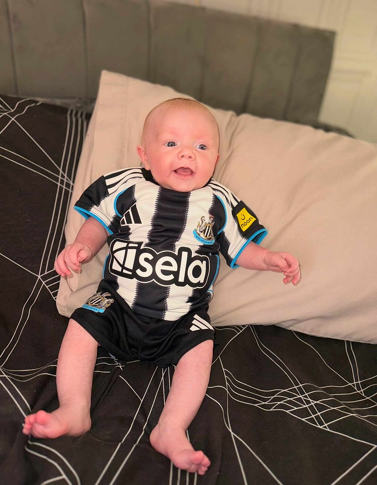 Ronniejay is registered to the contest to win money with this photo: baby, infant, smiling, bed, pillow, black_and_white, striped_shirt, soccer_jersey, clothing, happy, person, child, indoors, cute, young, feet, hands, head, face, sportswear
