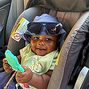 Elijah is registered to the contest to win money with this photo: accessory, baby, blue, car_interior, car_seat, child, clothing, cute, face, green, happy, hat, holding, infant, portrait, seat_belt, sitting, smile, sunglasses, toy