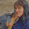 affection, collar, dog, eyes_closed, face, jacket, landscape, licking, long_hair, outdoor, pet, portrait, riverside, rocks, rottweiler, selfie, shoreline, smiling, water, woman