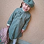accessory, beret, casual, child, concrete_floor, cute, fashion, footwear, girl, green_coat, happy, outdoor, person, pink_backpack, portrait, smiling, standing, wall, white_tights, young