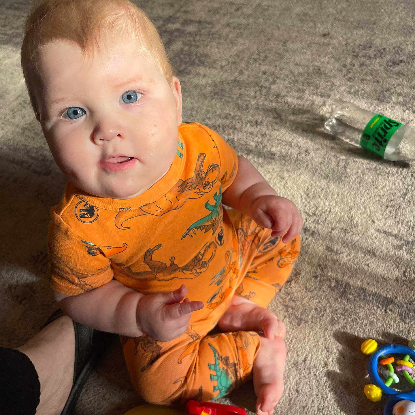 Zayden is registered to the contest to win money with this photo: baby, bodypart, bottle, clothing, couch, face, finger, footwear, furniture, hand, head, person, photography, portrait, sandal, shoe, sitting, t_shirt, toy, waterbottle