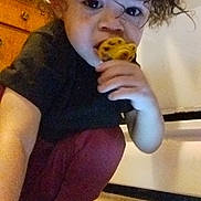 Christian is registered to the contest to win money with this photo: toddler, child, curly_hair, cookie, tablet, kitchen, floor, barefoot, crouching, indoor, brown_hair, black_shirt, red_pants, young_child, snack, technology, curious, light, home, person