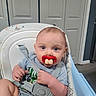 baby, high_chair, pacifier, blue_eyes, gray_clothing, indoor, infant, seatbelt, face, expression, child, cute, funny, furniture, room, door, human, portrait, baby_toy, humor
