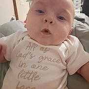 Ryker is registered to the contest to win money with this photo: baby, infant, onesie, face, expression, indoor, soft_surface, clothing, child, cute, person, portrait, newborn, skin, head, eyes, mouth, hand, blurred_background, light