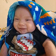 Ryker joined the competition — help win amazing prizes! baby, smiling, blanket, blue, indoor, child, toddler, clothing, shirt, baseball, pattern, face, happy, person, portrait, cozy, dreamcatcher, furniture, soft_lighting, cute