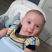 Ryker joined the competition — help win amazing prizes! baby, child, high_chair, bib, striped_clothing, blue_eyes, smile, indoor, person, face, infant, cute, happy, furniture, wood_floor, door, home, expression, young, curious