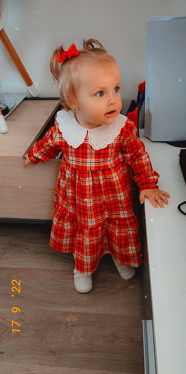 April a rejoint le concours — aidez-le/la à gagner de superbes lots ! baby_toddler_clothing, blond, child, dress, event, eye, face, fashion_design, flooring, hair, head, pattern, person, plaid, red, sitting, sleeve, sock, tartan, toddler
