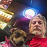Kona Marie is registered to the contest to win money with this photo: man, dog, pet, indoor, bar, television, bottle, drink, sign, casual_clothing, facial_hair, earrings, pink, polka_dot, leash, portrait, selfie, beard, light, ceiling