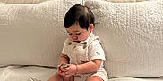 Gian is registered to the contest to win money with this photo: baby, child, infant, sitting, couch, quilt, white, soft, indoors, cute, hands, object, focused, clothing, shoes, hair, pillow, neutral_colors, home, portrait