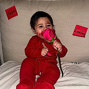 Gian joined the competition — help win amazing prizes! baby, red_onesie, rose, flower, lipstick_marks, face, couch, sticky_notes, happy, valentine, infant, child, smiling, holding, pink_rose, indoor, cute, person, sitting, bed