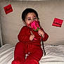 baby, red_onesie, rose, flower, lipstick_marks, face, couch, sticky_notes, happy, valentine, infant, child, smiling, holding, pink_rose, indoor, cute, person, sitting, bed