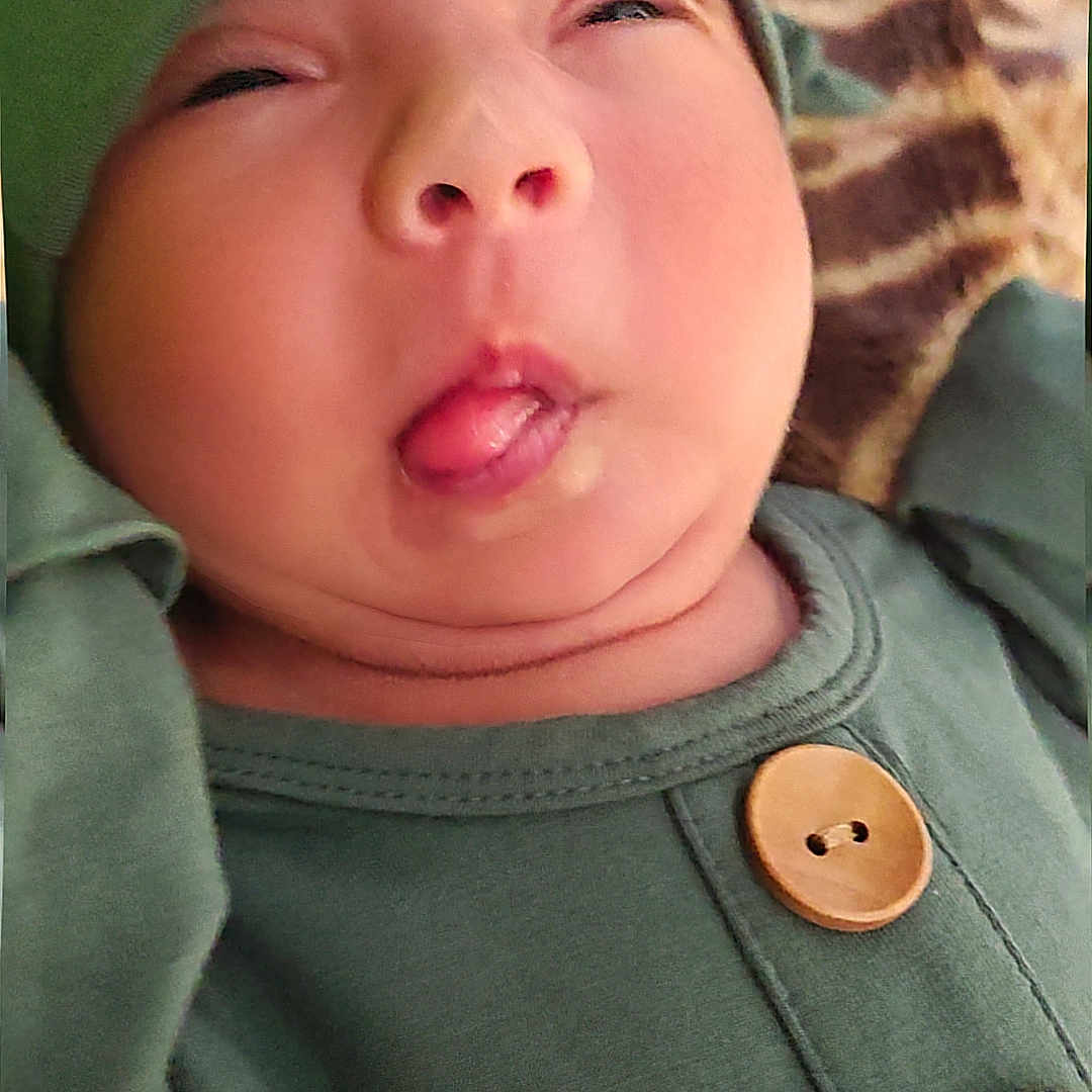 Milily is registered to the contest to win money with this photo: baby, infant, green_clothing, hat, tongue_out, funny_face, cute, child, portrait, buttoned_shirt, closeup, expression, skin, headwear, indoors, person, young_child, face, silly, squinting_eyes