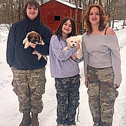 Mr. Knox joined the competition — help win amazing prizes! boots, camouflage_pants, dog, family_photo, group, holding_pet, hoodie, outdoor, person, pet, puppy, red_barn, rural, smiling, sneakers, snow, snowy_path, sweater, trees, winter