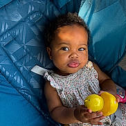Noor Nala is registered to the contest to win money with this photo: baby, child, toy, yellow_duck, blue_cushion, seat, curly_hair, smiling, portrait, infant, clothing, floral_dress, sitting, indoors, face, hand, cute, playful, happiness, soft_light