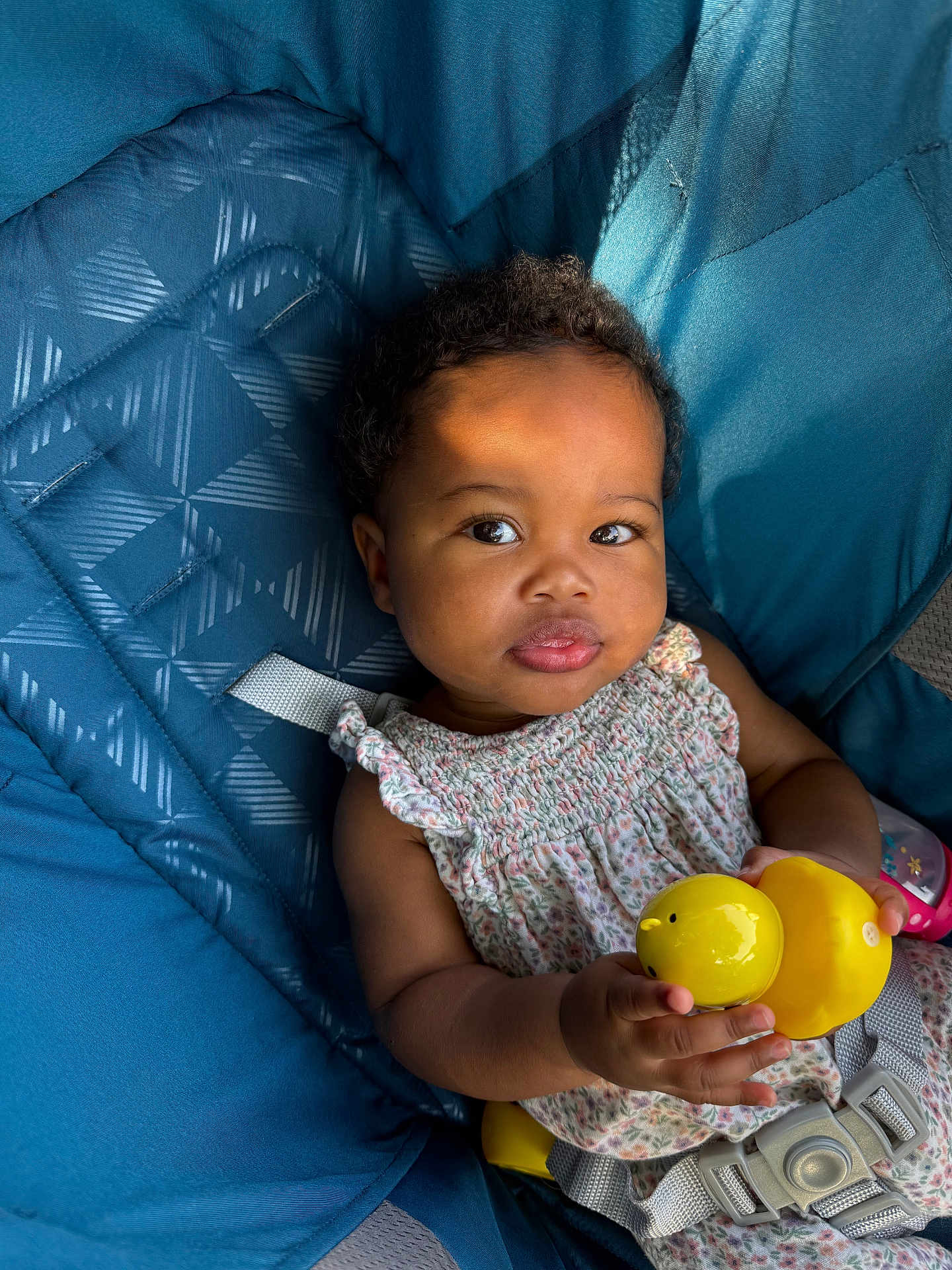 Noor Nala is registered to the contest to win money with this photo: baby, child, toy, yellow_duck, blue_cushion, seat, curly_hair, smiling, portrait, infant, clothing, floral_dress, sitting, indoors, face, hand, cute, playful, happiness, soft_light