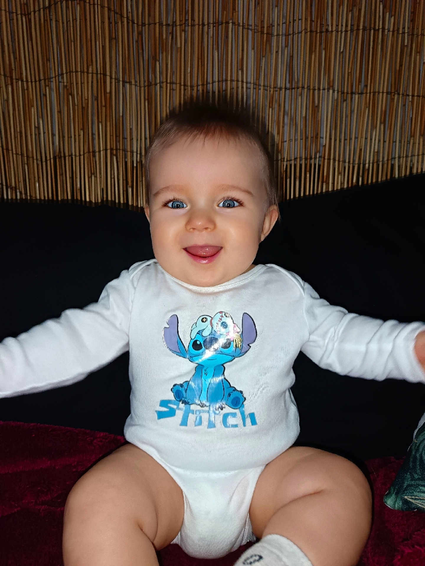 Izao participe au concours pour gagner de l'argent avec cette photo : baby, child, smiling, blue_eyes, onesie, stitch, animated_character, sitting, indoor, cushion, bamboo_wall, happy, cute, portrait, infant, clothing, person, face, expression, long_sleeve