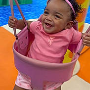 Ivyannah is registered to the contest to win money with this photo: toddler, child, swing, playground, pink_crown, pink_clothing, smiling, happy, indoor_play_area, colorful, play_equipment, legs, headband, baby, fun, joy, person, cute, active, motion
