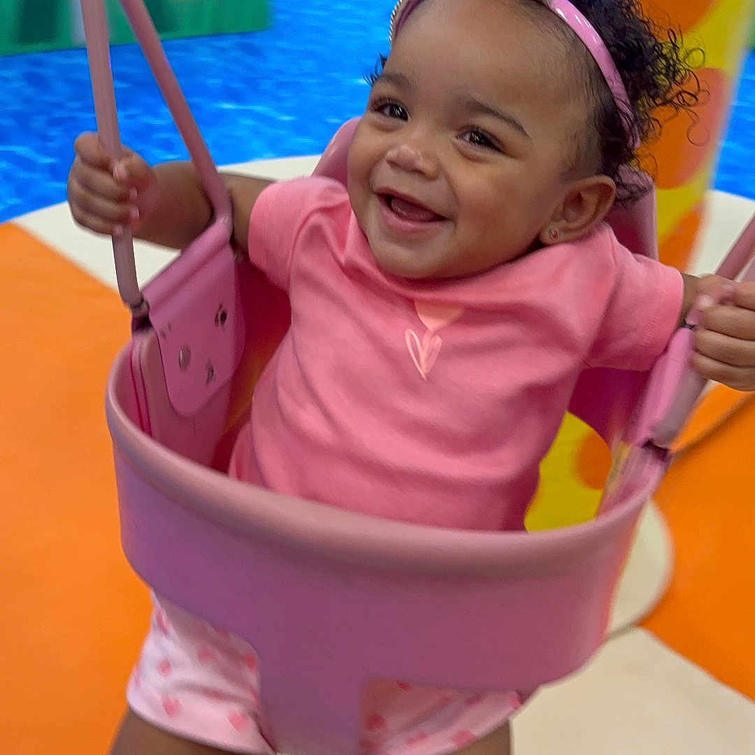 Ivyannah is registered to the contest to win money with this photo: toddler, child, swing, playground, pink_crown, pink_clothing, smiling, happy, indoor_play_area, colorful, play_equipment, legs, headband, baby, fun, joy, person, cute, active, motion
