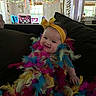 Eleonor joined the competition — help win amazing prizes! baby, child, feather_boa, yellow_headband, smiling, couch, indoor, party_decorations, colorful, happy, portrait, person, festive, headwear, furniture, window, curtains, bright, decor, celebration