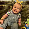 Eleonor is registered to the contest to win money with this photo: baby, child, smiling, headband, overalls, striped_shirt, bracelets, green_couch, toy, plush, indoor, happy, cute, infant, sitting, colorful, playful, portrait, young, person