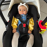 Maddy a rejoint le concours — aidez-le/la à gagner de superbes lots ! baby, child, car_seat, headband, yellow_sweater, white_tights, blue_eyes, indoor, floor, straps, sitting, portrait, cute, infant, clothing, person, seat, comfort, looking_at_camera, baby_toy