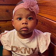 Samira is registered to the contest to win money with this photo: baby, child, chubby_arms, closeup, clothing, curious_expression, cute, dkny_shirt, face, flower, headwear, indoors, infant, person, pink_headband, portrait, sitting, skin, wooden_background, young_child