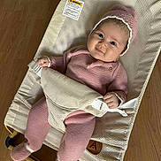 Hanna is registered to the contest to win money with this photo: baby, infant, pink_outfit, knitwear, baby_bouncer, mesh, wooden_floor, smile, cute, hat, cozy, child, indoor, comfortable, relaxed, adorable, person, footwear, seated, baby_clothing