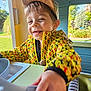boy, cap, casual_clothing, child, close_up, daylight, face, fun, greenery, hand, happy, indoor, play_kitchen, playing, portrait, smiling, toy, window, yellow_jacket, young
