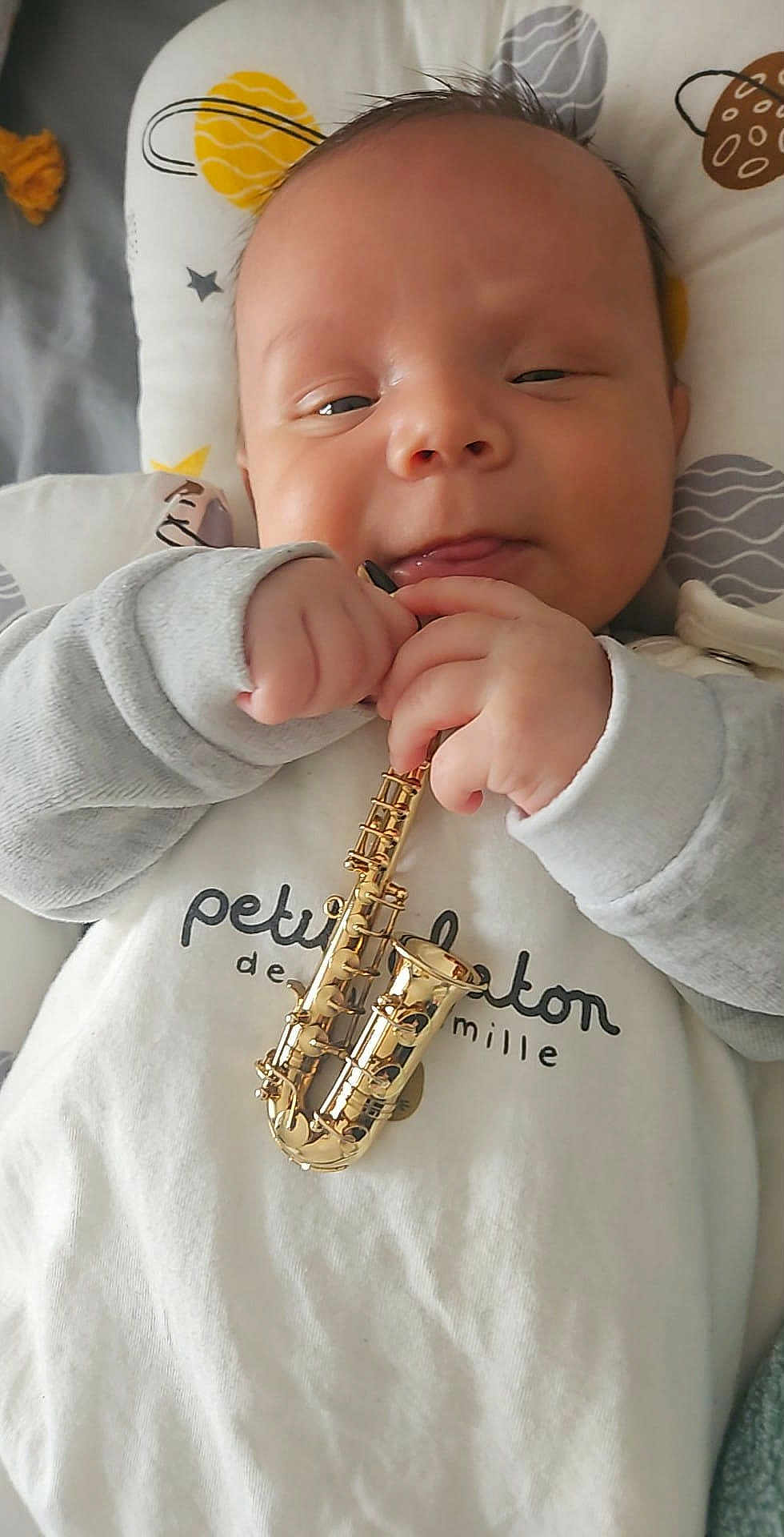David Bogdan a rejoint le concours — aidez-le/la à gagner de superbes lots ! baby, infant, toy, saxophone, musical_instrument, hand, face, clothing, sleepy, cute, indoors, bed, pillow, blanket, expression, young_child, small, cozy, closeup, holding