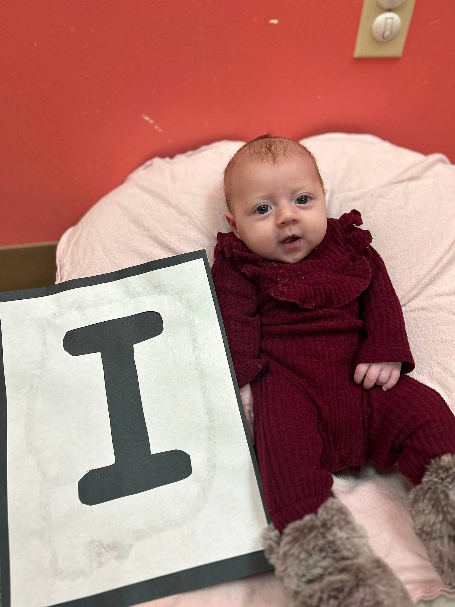 Juliette is registered to the contest to win money with this photo: baby, baby_toddler_clothing, child, comfort, cross, font, fun, fur, happy, hoodie, number, person, religious_item, room, sign, sitting, sleeve, standing, symbol, t_shirt