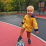 toddler, child, soccer_ball, yellow_jacket, outdoor, playground, autumn, trees, fence, court, sport, smiling, shoes, pants, recreation, activity, fun, daylight, park, happy