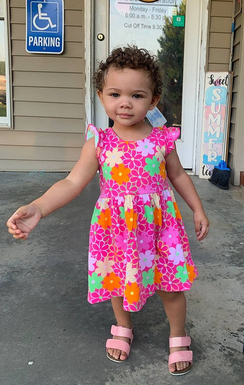 Lydia is registered to the contest to win money with this photo: baby_toddler_clothing, door, dress, facial_expression, fashion, hairstyle, happy, head, joint, magenta, one_piece_garment, person, pink, public_space, purple, shoulder, skin, sleeve, standing, textile