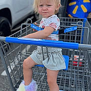 Makayla is registered to the contest to win money with this photo: blond_hair, car, child, clothing, face, fluffy_shoes, outdoor, parking_lot, portrait, pouting, rainbow_colors, shirt, shopping_cart, shorts, sitting, store, toddler, truck, vehicle, walmart