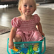 Makayla is registered to the contest to win money with this photo: child, toddler, girl, smiling, portrait, sitting, toy_basket, shopping_basket, toys, pink_dress, indoors, living_room, wooden_floor, sofa, playtime, blonde_hair, ponytail, happy, family_home, photography