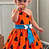 Makayla joined the competition — help win amazing prizes! barefoot, blue_sash, bow, child, costume, girl, hair_accessory, halloween, indoors, orange_dress, portrait, pumpkin_pattern, shoes, smiling, snack, standing, toddler, walking, window_blinds, wood_floor