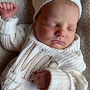 James is registered to the contest to win money with this photo: baby, newborn, sleeping, knitted_hat, knitted_sweater, white_clothing, infant, soft_blanket, peaceful, closeup, portrait, cute, child, resting, cozy, tiny_fingers, face, sleep, warm, soft_texture