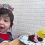 birthday_crown, brick_wall, cake, celebration, child, chocolate_cake, cute, denim_overalls, dessert, face, food, girl, happy, indoor, person, plate, red_shirt, smiling, table, young_child
