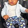 baby, infant, child, car_seat, portrait, sitting, indoors, face, eyes, looking_at_camera, curly_hair, hoodie, white_clothing, pajamas, dinosaur_pattern, smiling, car_seat_safety, black_background, close_up, photography